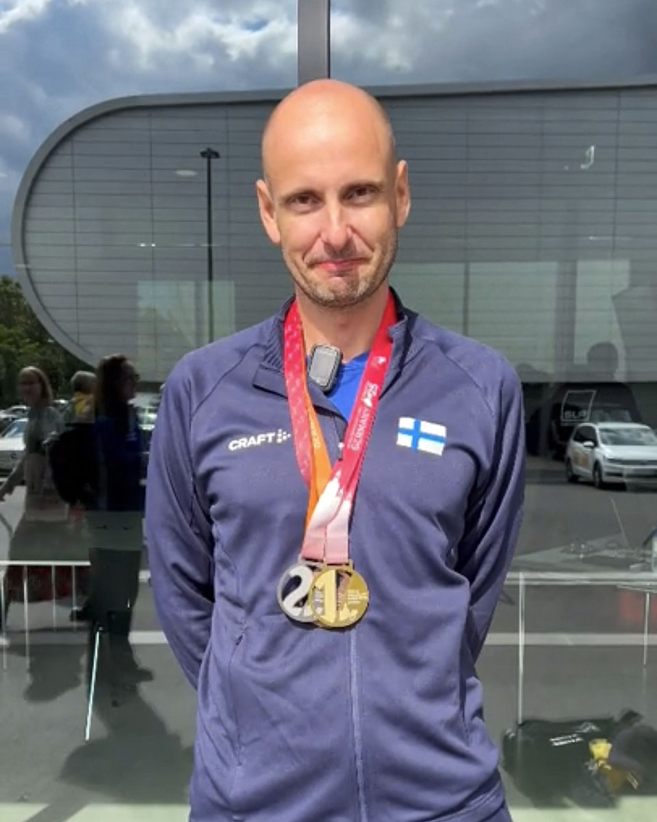 Tommi Räisänen lähikuvassa stadionin edustalla mitalit kaulassaan.